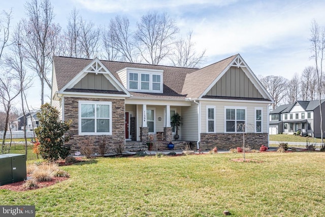 craftsman-style house featuring stone siding, roof with shingles, board and batten siding, covered porch, and a front yard