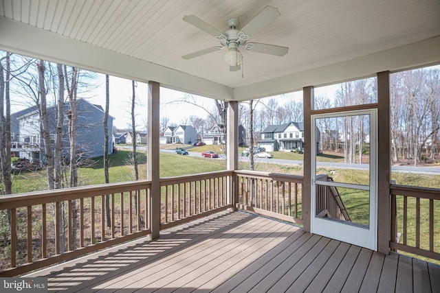 unfurnished sunroom with a ceiling fan, a residential view, and a wealth of natural light