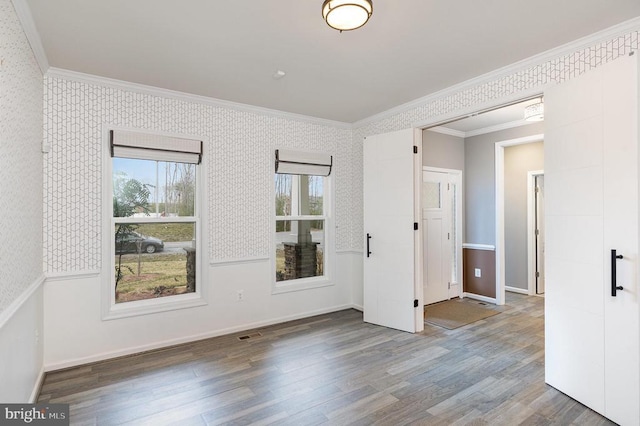 empty room with wallpapered walls, baseboards, ornamental molding, wainscoting, and wood finished floors