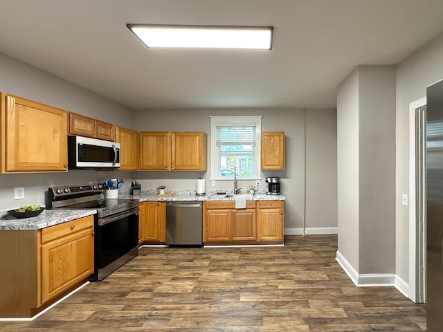 kitchen with stainless steel appliances, sink, light stone counters, and dark hardwood / wood-style flooring