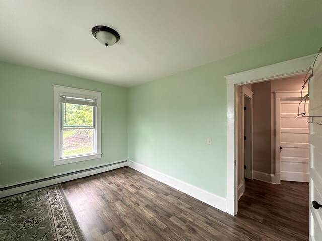 empty room with baseboard heating and dark hardwood / wood-style flooring