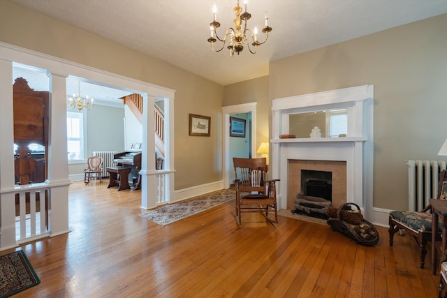 living area with a fireplace, radiator, light wood-type flooring, and a notable chandelier