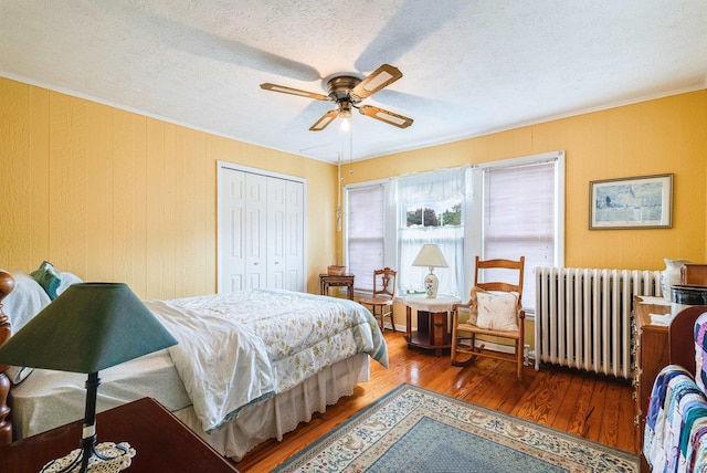 bedroom with a textured ceiling, radiator heating unit, a closet, hardwood / wood-style flooring, and ceiling fan