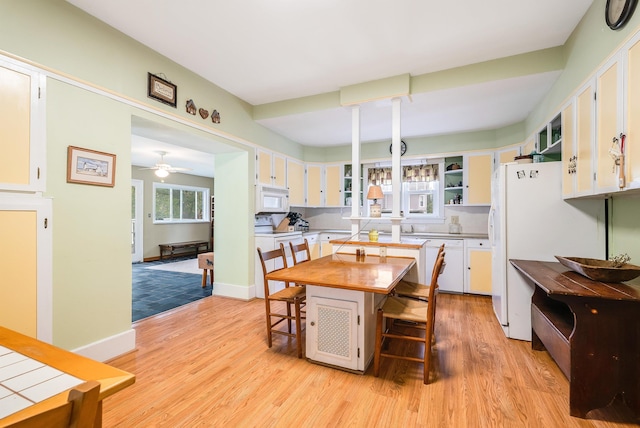 kitchen with a breakfast bar area, a kitchen island, white appliances, light hardwood / wood-style floors, and white cabinets