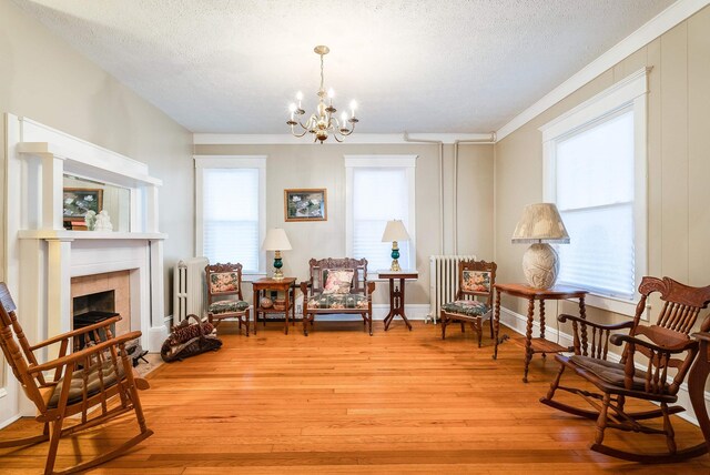 sitting room featuring a notable chandelier, radiator heating unit, a fireplace, and light wood-type flooring