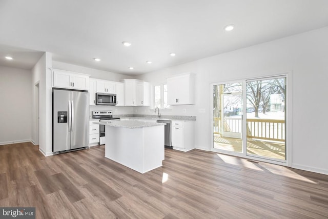 kitchen featuring a kitchen island, appliances with stainless steel finishes, white cabinets, hardwood / wood-style flooring, and light stone countertops