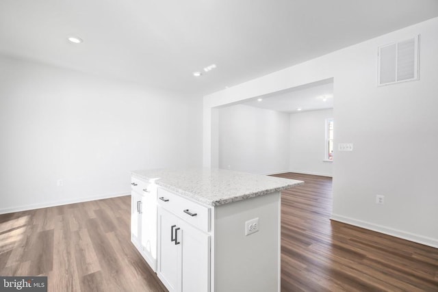 kitchen with light stone counters, hardwood / wood-style flooring, a kitchen island, and white cabinets