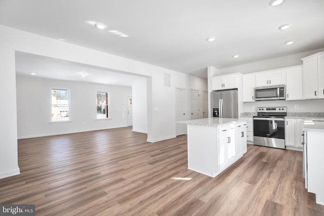 kitchen featuring white cabinetry, light stone counters, wood-type flooring, appliances with stainless steel finishes, and a kitchen island