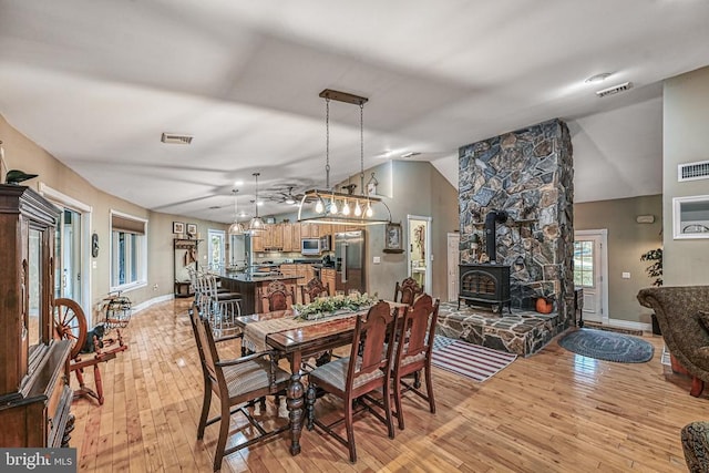 dining area featuring lofted ceiling, visible vents, baseboards, light wood finished floors, and a wood stove