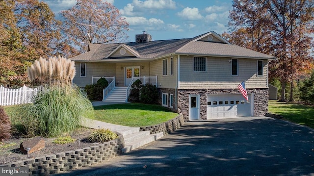 view of front of home with driveway, stone siding, an attached garage, and a front lawn