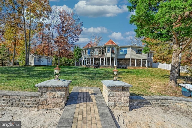 back of property with a yard, fence, a deck, stone siding, and an outdoor structure