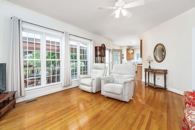 living area with visible vents, a ceiling fan, light wood-style floors, and baseboards