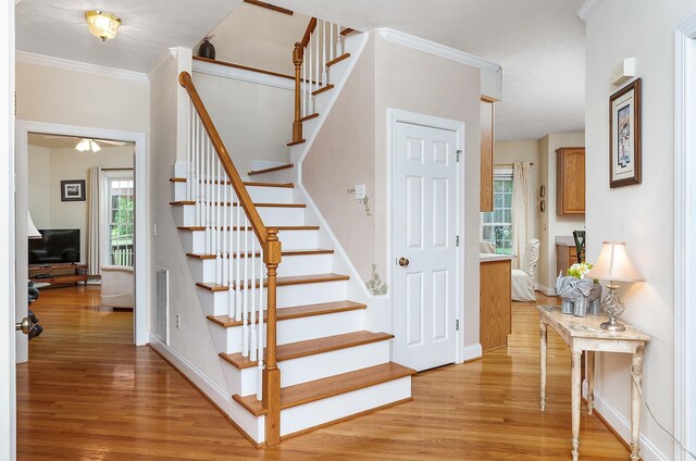 staircase featuring crown molding, baseboards, wood finished floors, and visible vents