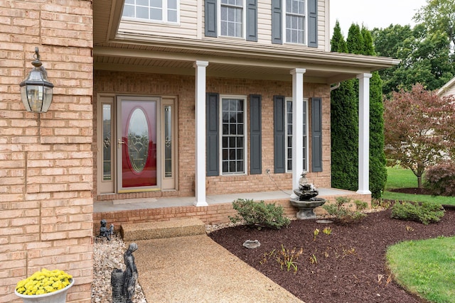 doorway to property featuring covered porch and brick siding
