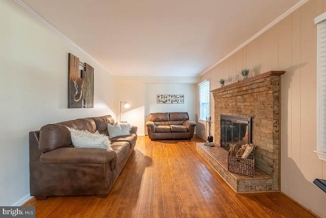 living area with light wood-type flooring, a brick fireplace, baseboards, and crown molding