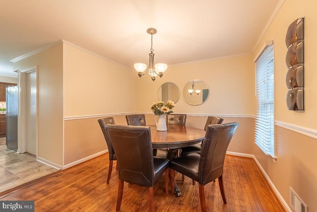 dining area featuring visible vents, ornamental molding, wood finished floors, a chandelier, and baseboards