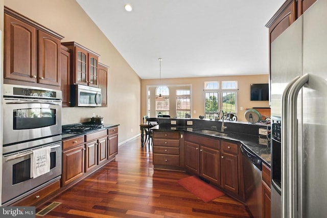 kitchen featuring sink, dark wood-type flooring, stainless steel appliances, decorative light fixtures, and dark stone counters