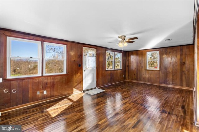 interior space with ceiling fan, wooden walls, and dark hardwood / wood-style flooring