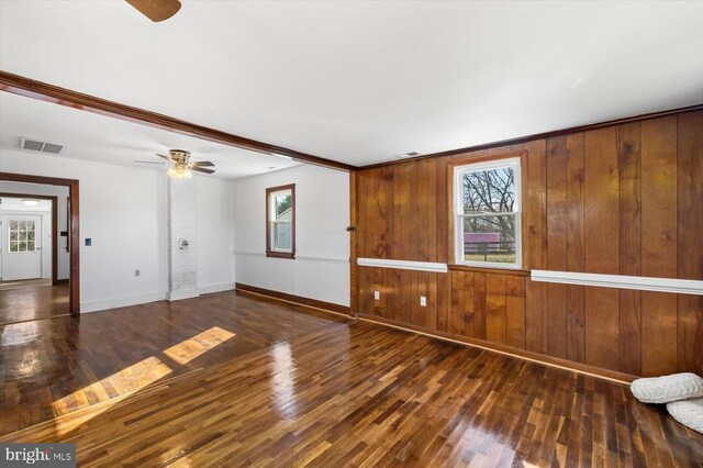 empty room with dark hardwood / wood-style flooring, plenty of natural light, ceiling fan, and wood walls