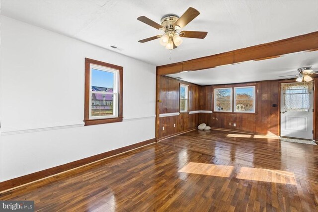 empty room featuring dark wood-type flooring, ceiling fan, and wood walls