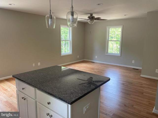 kitchen featuring dark stone countertops, hanging light fixtures, a center island, a healthy amount of sunlight, and white cabinets