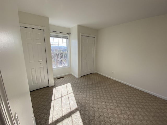 unfurnished bedroom with visible vents, baseboards, carpet floors, and multiple closets