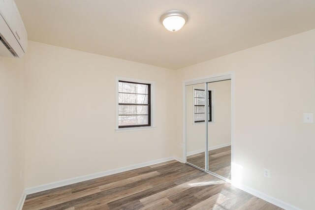 unfurnished bedroom with hardwood / wood-style flooring, a closet, and an AC wall unit