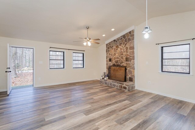 unfurnished living room with ceiling fan, a stone fireplace, vaulted ceiling, and wood-type flooring