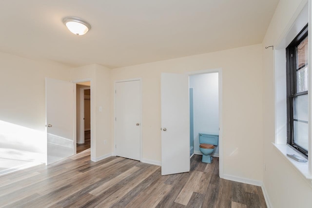 unfurnished bedroom with ensuite bathroom, hardwood / wood-style floors, and multiple windows