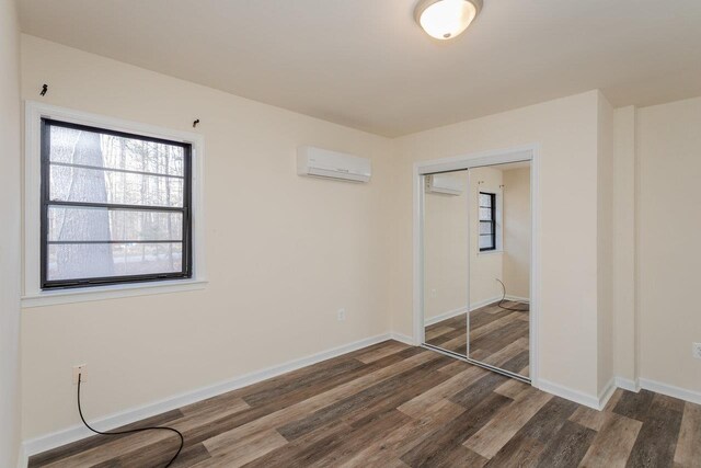 unfurnished bedroom featuring dark hardwood / wood-style flooring, a wall unit AC, and a closet