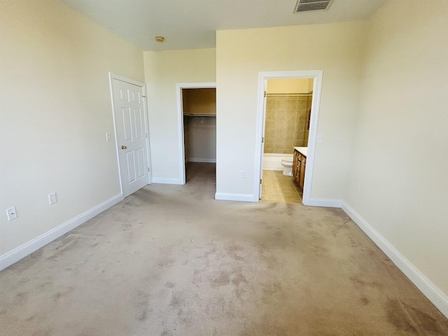 unfurnished bedroom featuring light colored carpet, ensuite bathroom, a spacious closet, and a closet