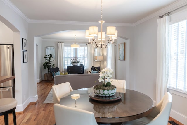 dining space featuring a healthy amount of sunlight, wood-type flooring, a chandelier, and ornamental molding