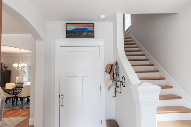 stairway with crown molding, hardwood / wood-style floors, and a chandelier