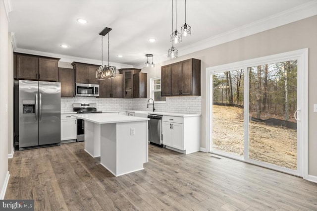 kitchen with appliances with stainless steel finishes, crown molding, dark brown cabinets, light countertops, and backsplash