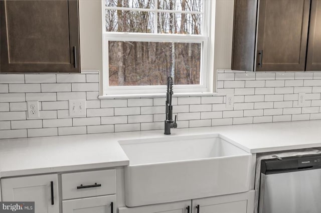 kitchen view of dark brown cabinetry, decorative backsplash, stainless steel dishwasher, a sink, and light countertops