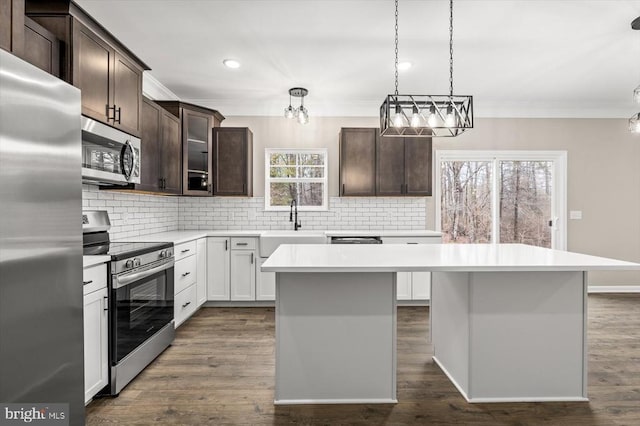 kitchen with stainless steel appliances, a center island, a chandelier, ornamental molding, and light countertops