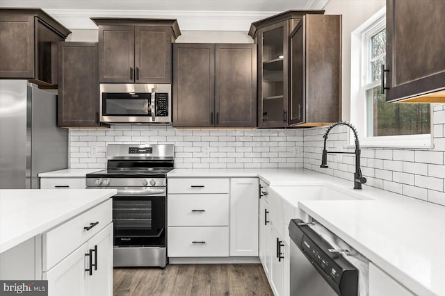 kitchen with appliances with stainless steel finishes, dark brown cabinets, light countertops, a sink, and dark wood finished floors