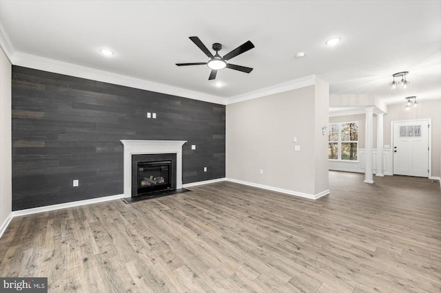 unfurnished living room with decorative columns, ceiling fan, ornamental molding, baseboards, and wood finished floors