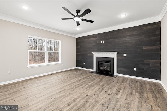 unfurnished living room featuring crown molding, a ceiling fan, baseboards, a fireplace with flush hearth, and wood finished floors