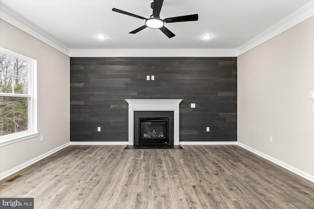 unfurnished living room featuring ornamental molding, baseboards, a ceiling fan, a fireplace with flush hearth, and wood finished floors
