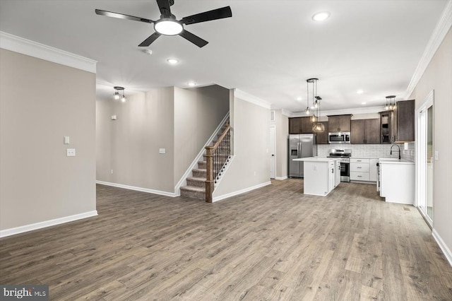 unfurnished living room with crown molding, ceiling fan, recessed lighting, stairs, and wood finished floors