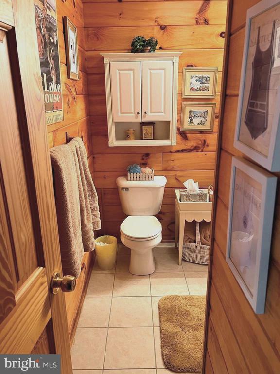 half bathroom with tile patterned floors, toilet, and wooden walls