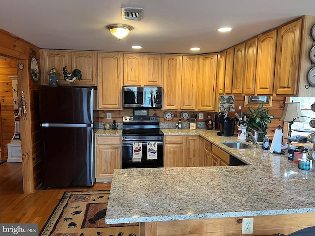kitchen with a peninsula, light wood finished floors, a sink, light stone countertops, and black appliances