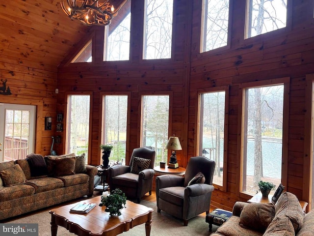 living area featuring a chandelier, wood walls, a healthy amount of sunlight, and high vaulted ceiling