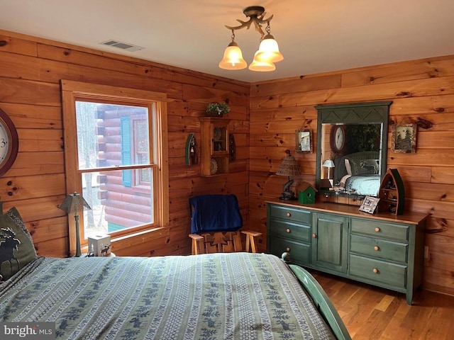 bedroom featuring light wood-style floors, wood walls, and visible vents