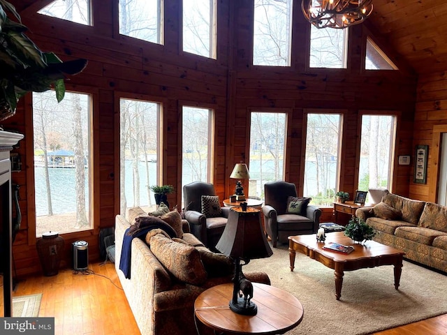 living area with wooden walls, a healthy amount of sunlight, high vaulted ceiling, and wood-type flooring