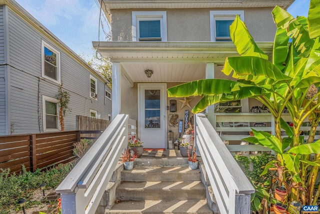 doorway to property featuring stucco siding and fence