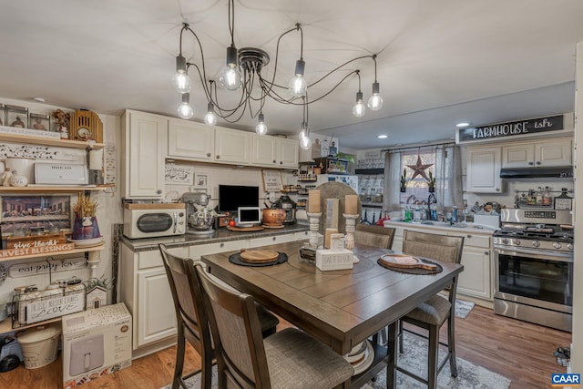 kitchen featuring under cabinet range hood, a chandelier, gas range, hanging light fixtures, and light wood-style floors