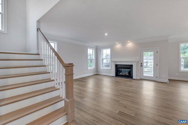 unfurnished living room featuring recessed lighting, baseboards, a glass covered fireplace, stairs, and wood finished floors