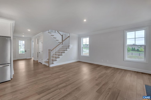 unfurnished living room featuring plenty of natural light, stairway, and ornamental molding